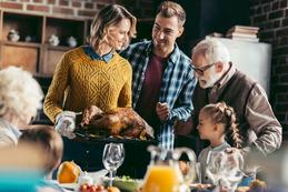 A family standing around the dinner table with turkey.